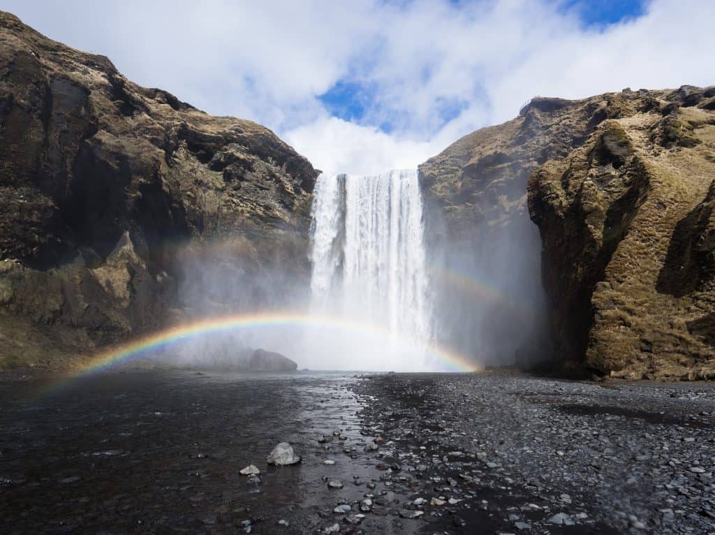 Skogafoss waterfall with a rainbow in the front on a sunny day.