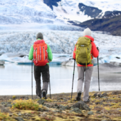 Two hikers in colorful jackets and backpacks walking with trekking poles toward a glacier in Iceland, showcasing the adventurous spirit of hiking in Iceland.